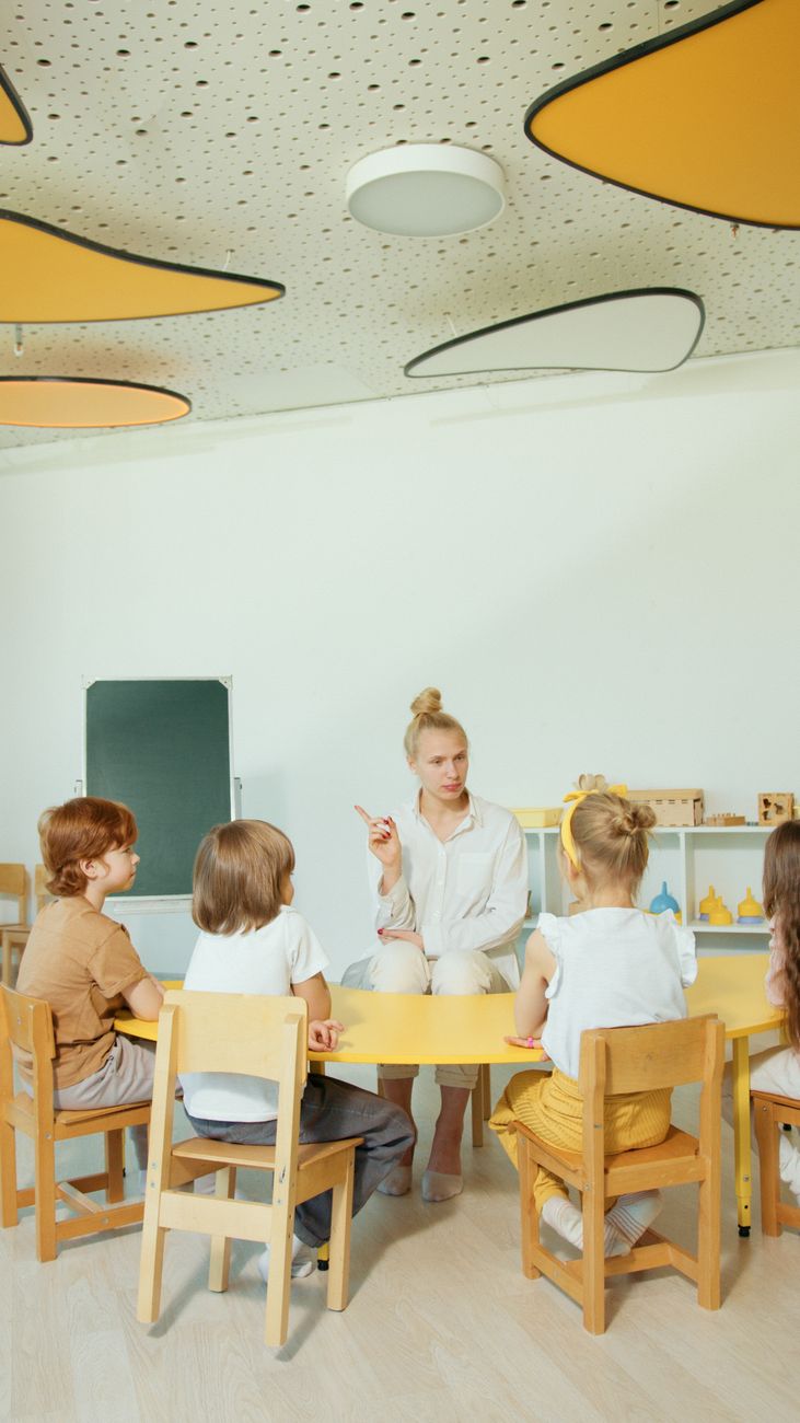 A teacher with children gathered around in a bright classroom